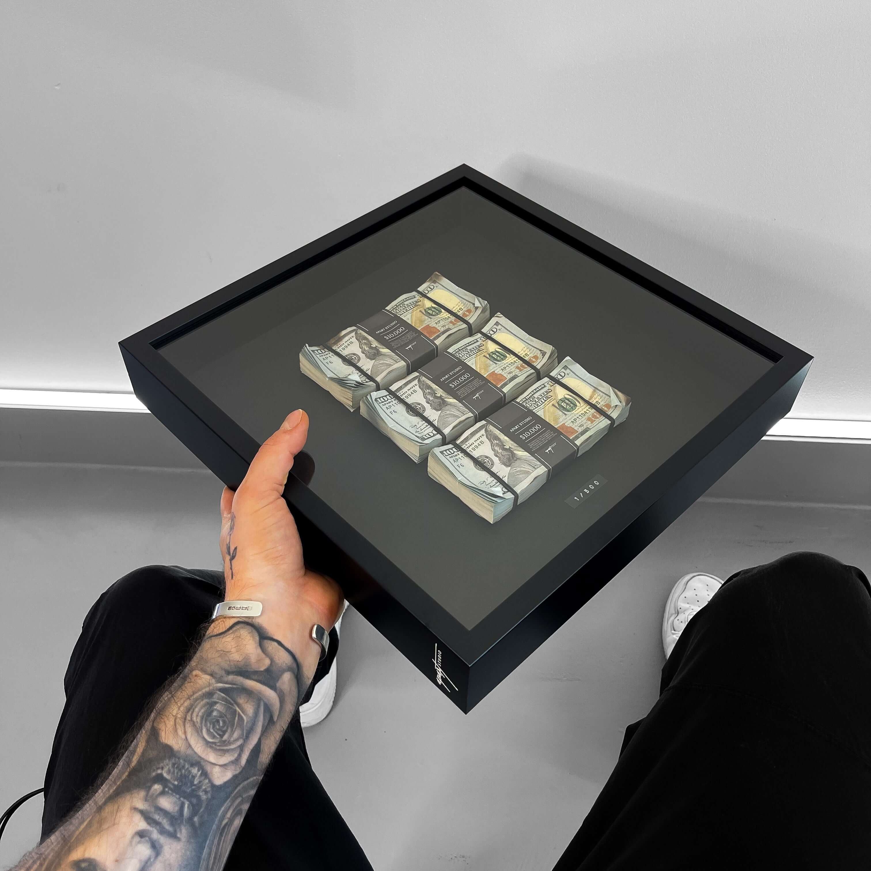 Person holding a framed artwork of dollar bills on a gray background
