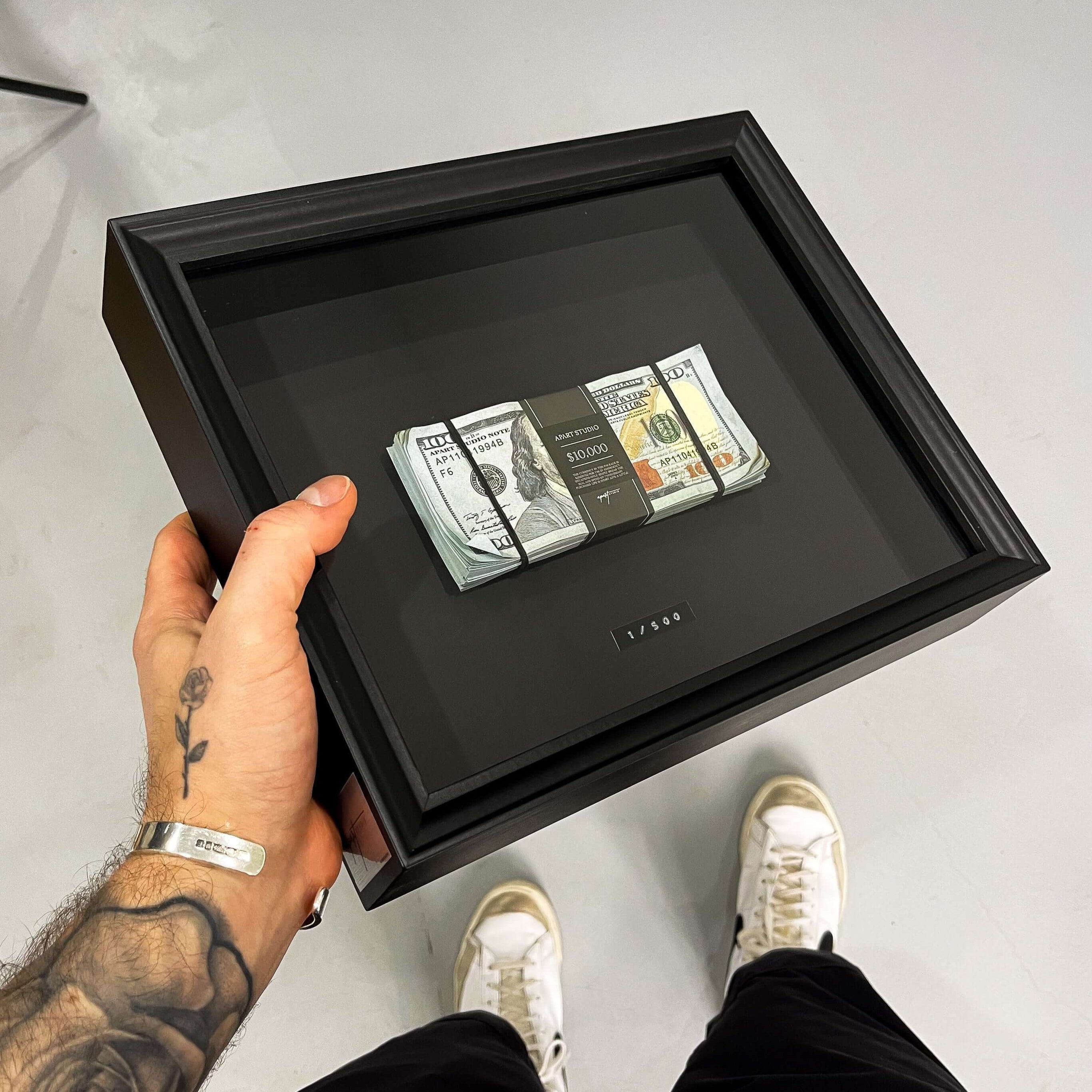 Person holding a black shadow box with money inside on a white floor.